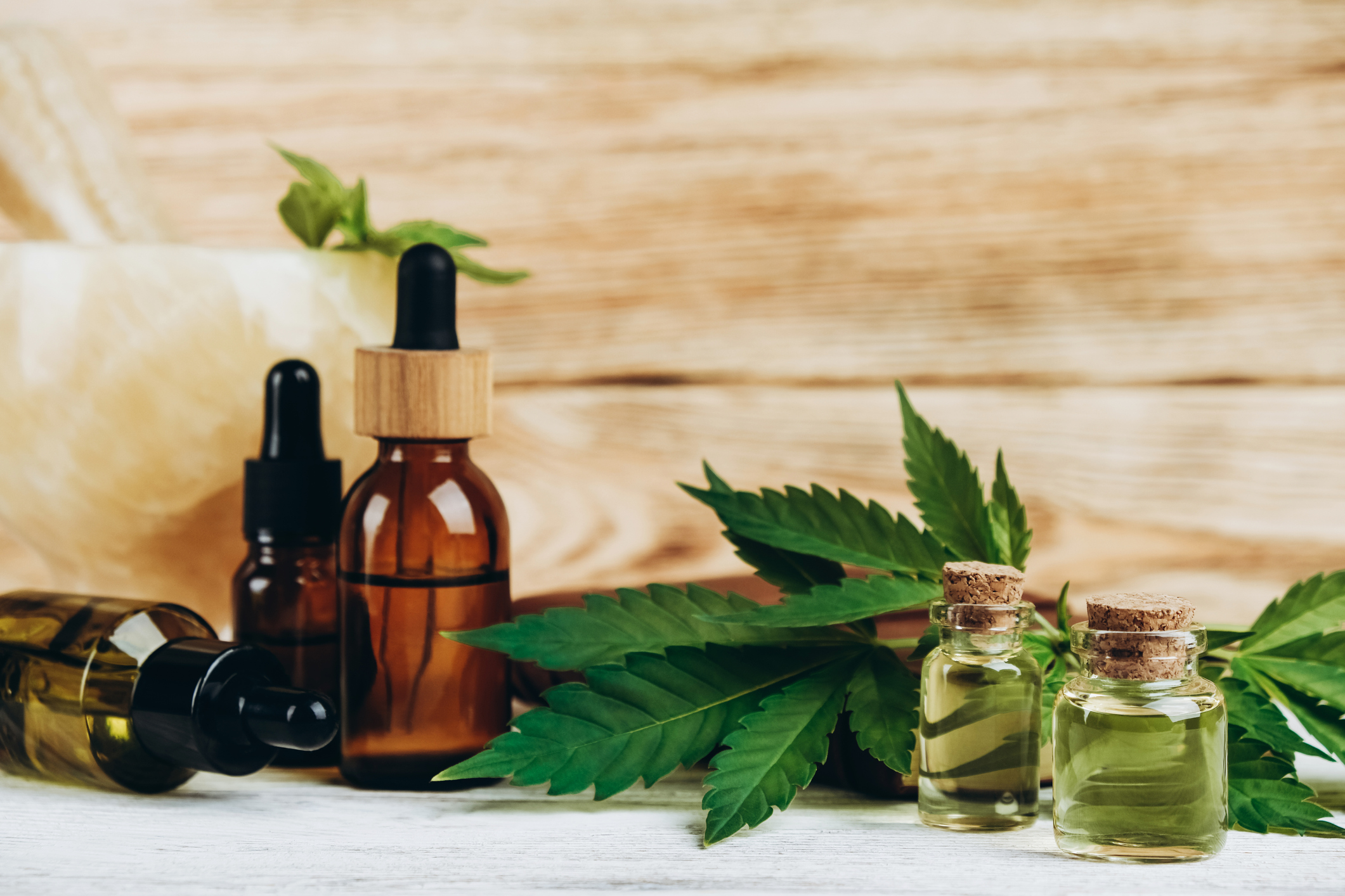 CBD oil in flacons, green cannabis, jade mortar and pestle against wooden wall close-up