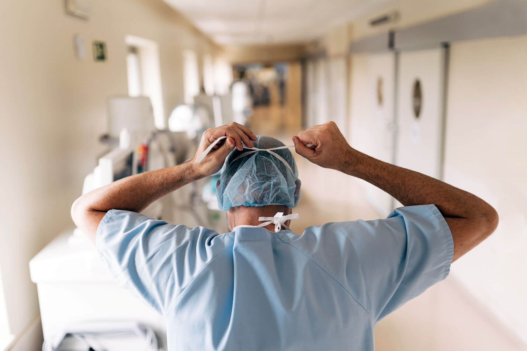 medical professional tying off face PPE from behind, looking down hospital corridor